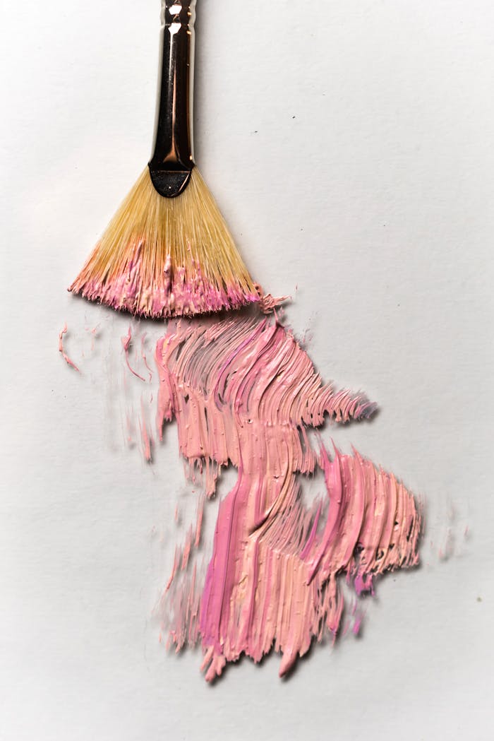 Close-up view of a fan paintbrush creating artistic pink brush strokes on a white canvas.
